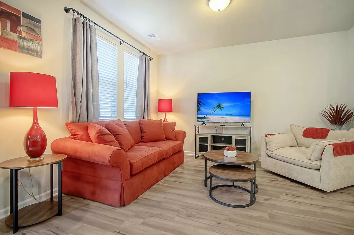 A cozy living room with a vibrant red sofa, a round coffee table, a decorative lamp, and a television. The space is set up for both relaxation and social activities, suggesting movie nights or board games with friends and family.