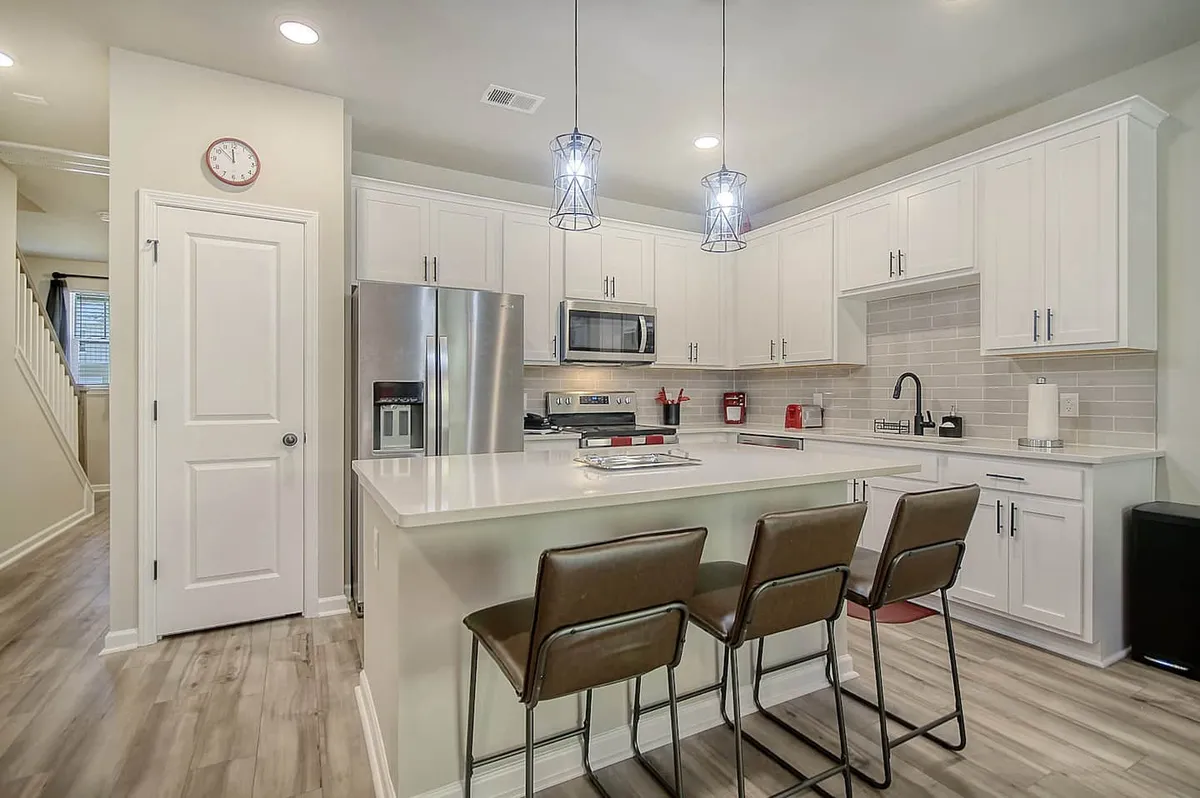 Bright and modern kitchen with a central island, stainless steel appliances, stylish light fixtures, and bar stools for casual seating. The layout is ideal for cooking, entertaining, or a relaxed morning coffee ritual.