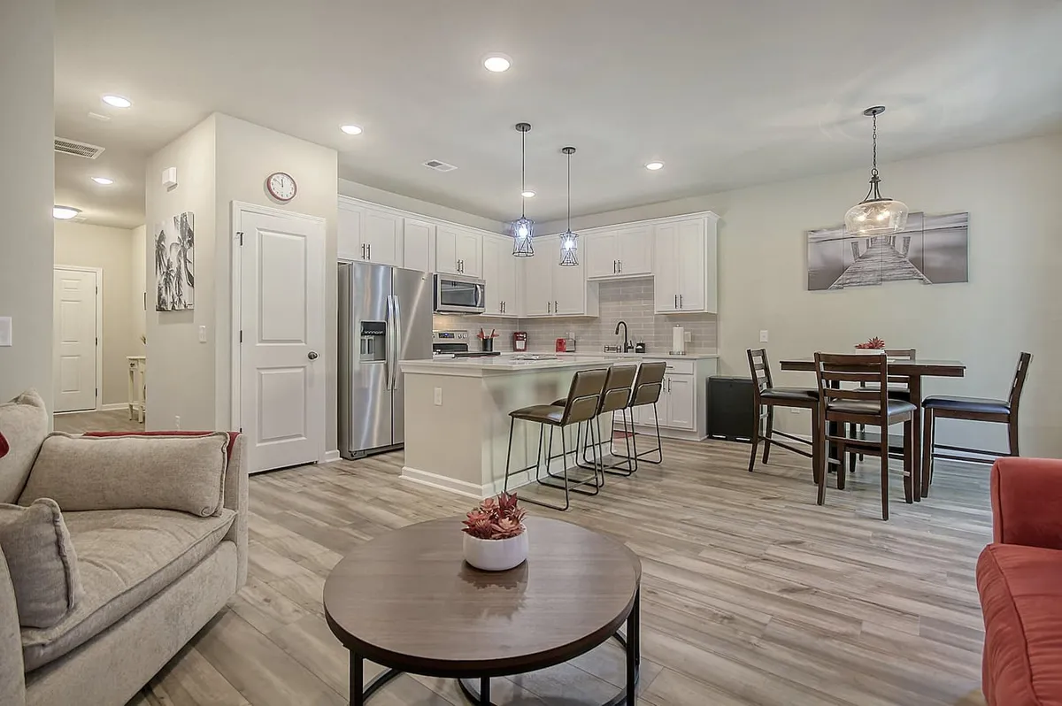This image showcases a cozy, open-concept interior featuring a kitchen island, dining table, and living room seating. The dining table is set in a central position, emphasizing a space for shared meals, while the kitchen island and modern appliances highlight the room’s functionality for cooking and gathering.