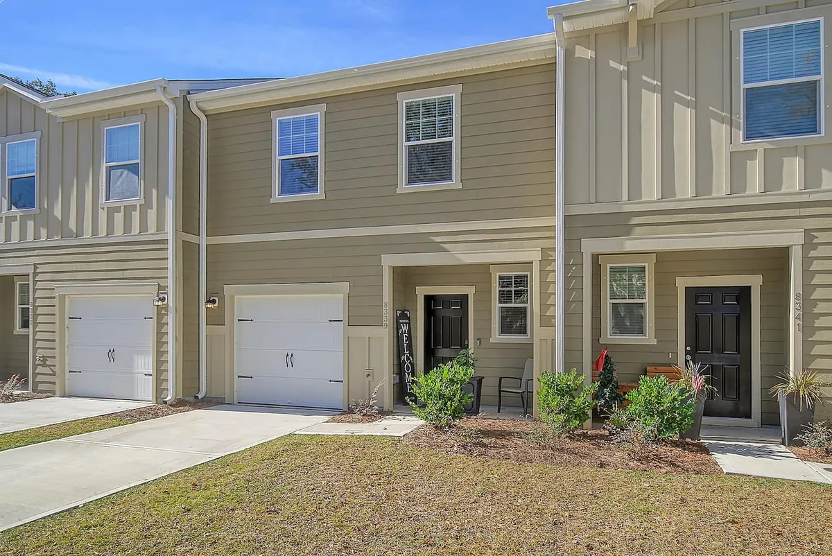 This image shows a welcoming exterior view of the home, with a front door, garage doors, attractive landscaping, and patio furniture. The scene suggests an inviting place to return to after a day exploring Charleston, with areas for gathering and relaxing outdoors.