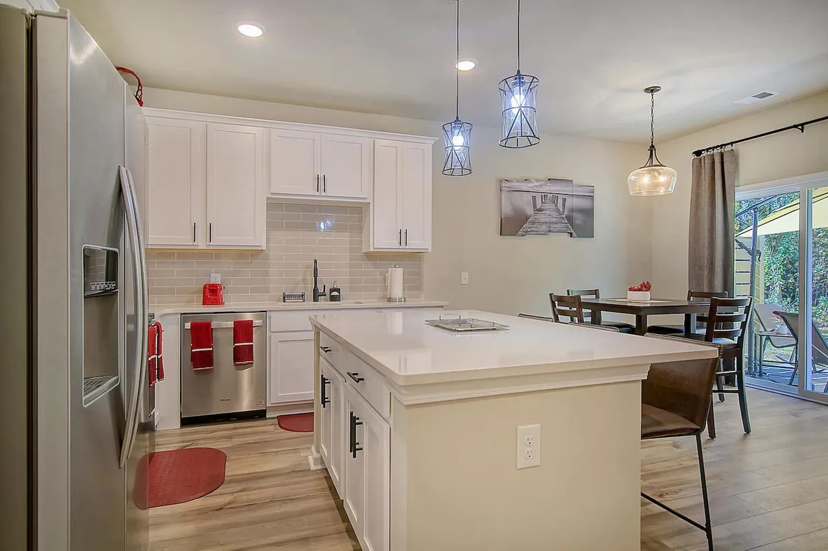 An open-plan kitchen and dining area with a central island, stainless steel appliances, pendant lighting, and comfortable seating. The room feels spacious and is ideal for multitasking—cooking, dining, and working all in one place.