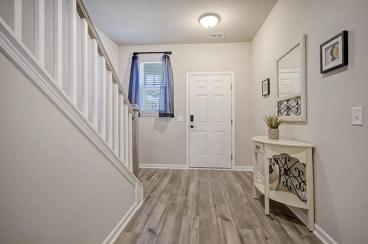 A welcoming front entryway with a staircase, console table, and natural light streaming through a window with soft curtains. The entry area feels inviting and sets a warm tone for the interior experience.