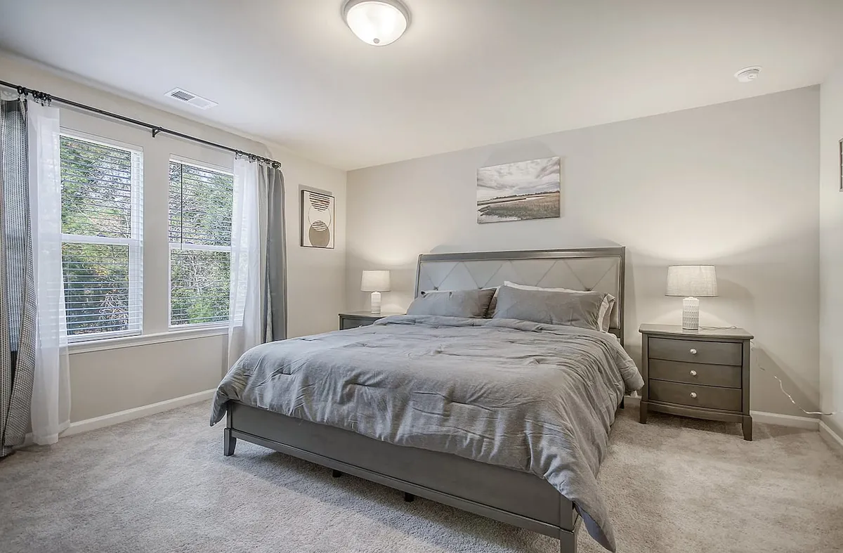 A tranquil bedroom with a plush bed, nightstands, large windows, and tasteful artwork. The setting exudes calm with its soft lighting and well-chosen decor, creating a perfect spot to unwind, nap, or appreciate the sunrise.