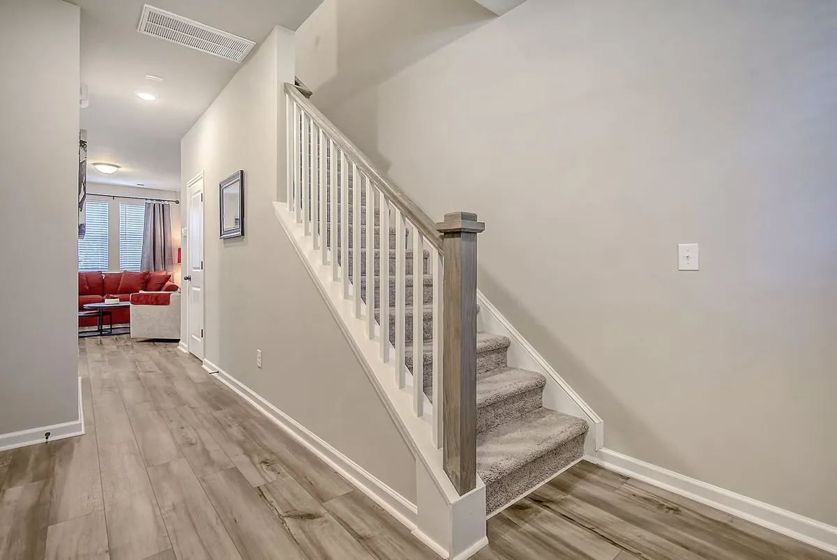 A view looking into the living room through a doorway, showcasing a modern staircase and stylish light fixtures. The living area appears spacious yet cozy, with hints of comfortable seating visible from the entry.
