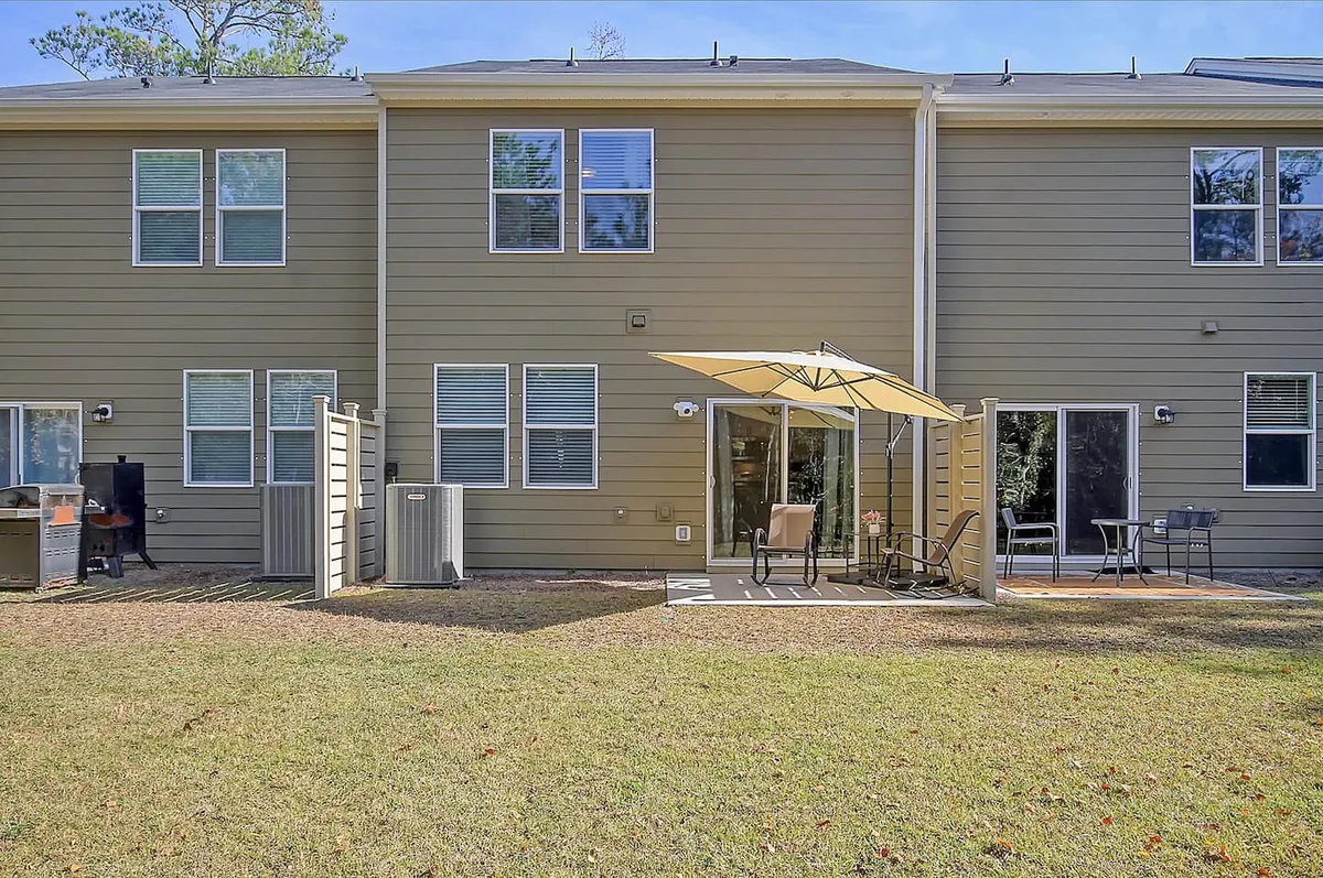 A backyard patio area with an umbrella, outdoor seating, and a lawn, set against the backdrop of the house’s windows. The space feels casual and welcoming, ideal for informal gatherings, dining, or relaxing in the sun.